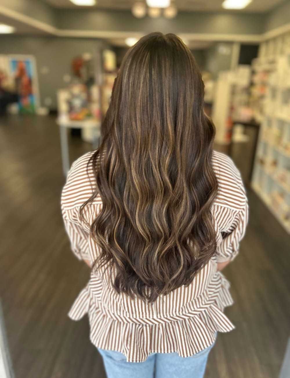 Long wavy brown hair with highlights cascading down a woman's back in a salon setting.