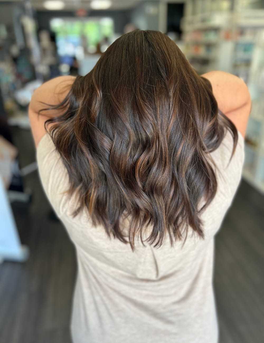 Back view of a woman with wavy, medium-length brown hair in a salon setting.