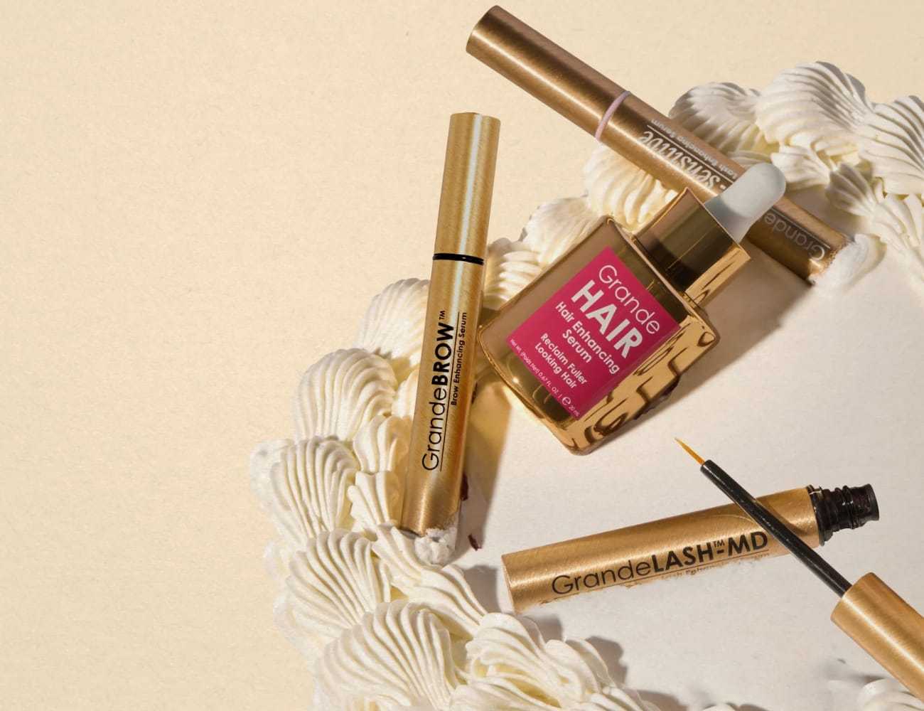 Cosmetic products on a table, including mascara and hair serum, with decorative cream swirls.