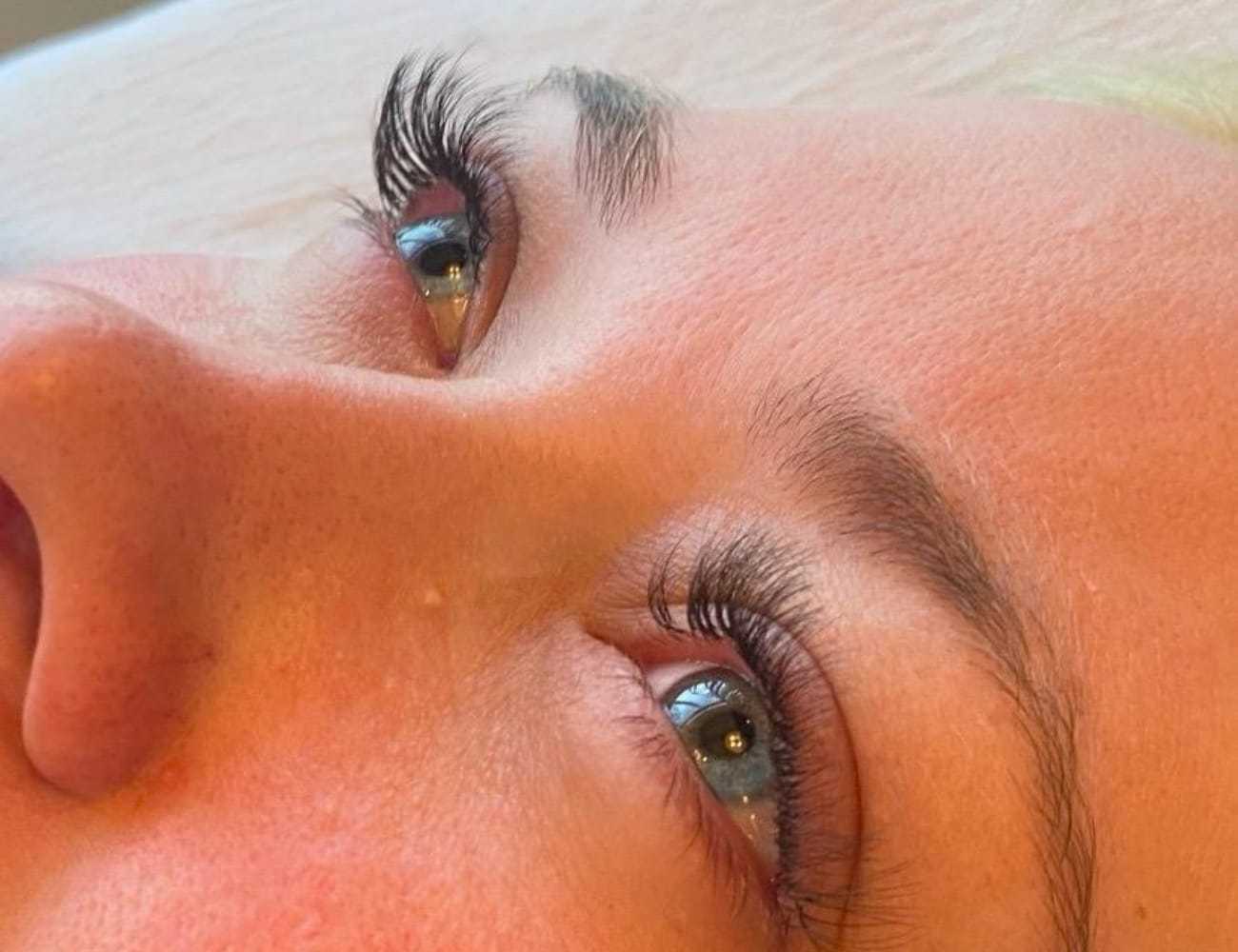 Close-up of a person's face with long, curled eyelashes and a neutral expression.