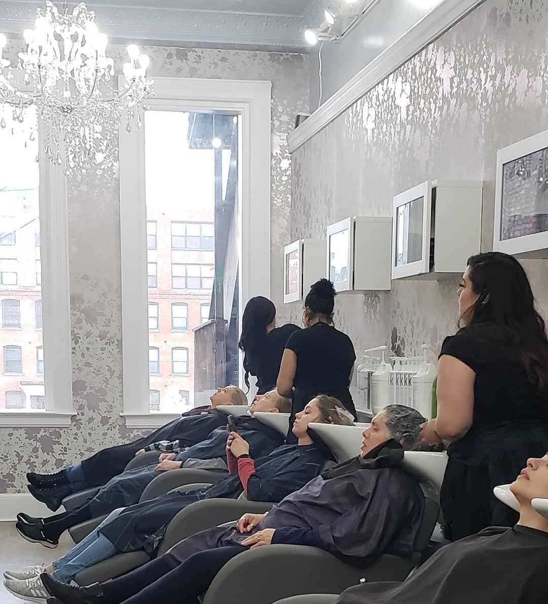 Salon interior with clients receiving hair treatments under a chandelier.