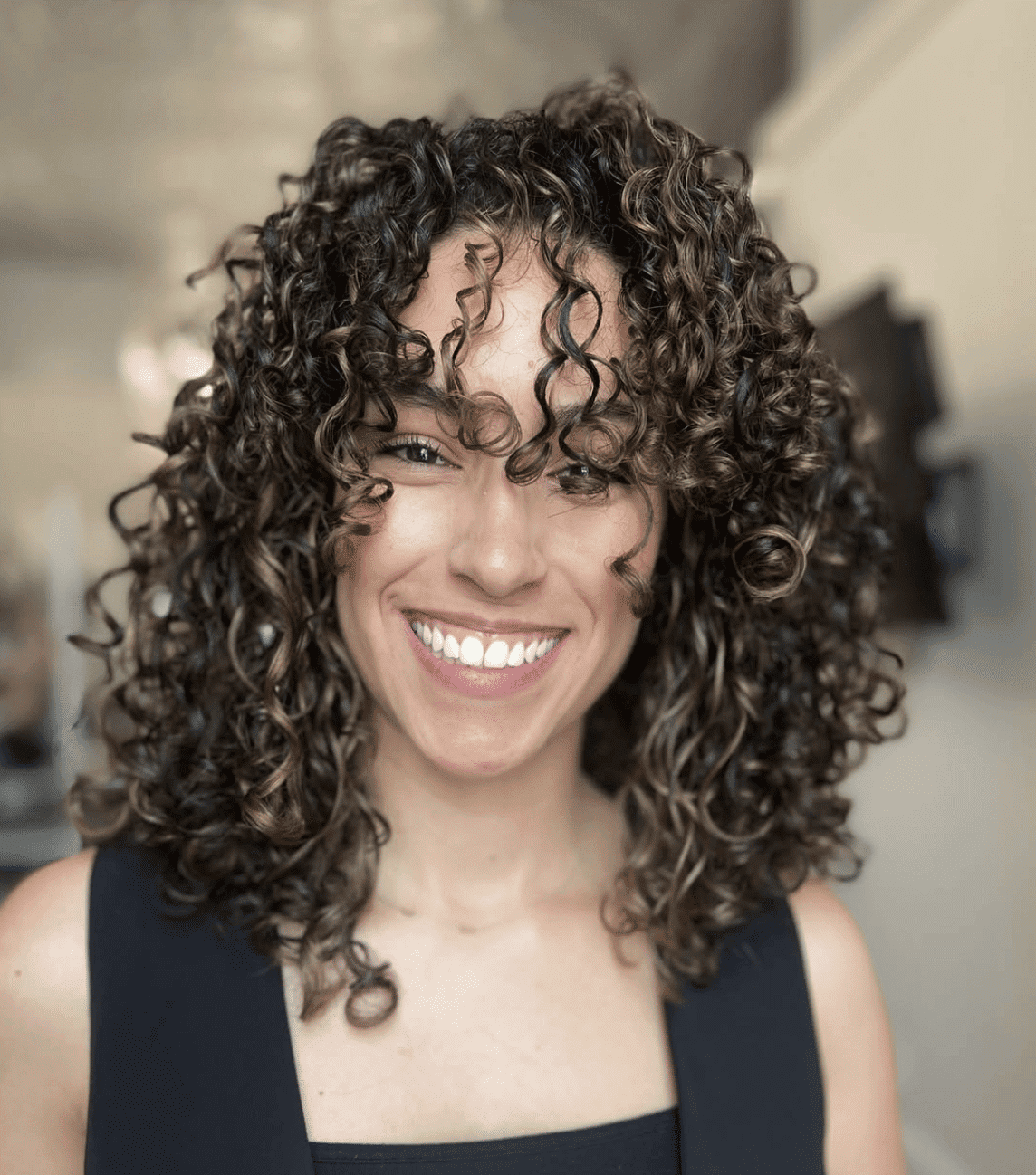 Smiling person with curly hair wearing a sleeveless black top.