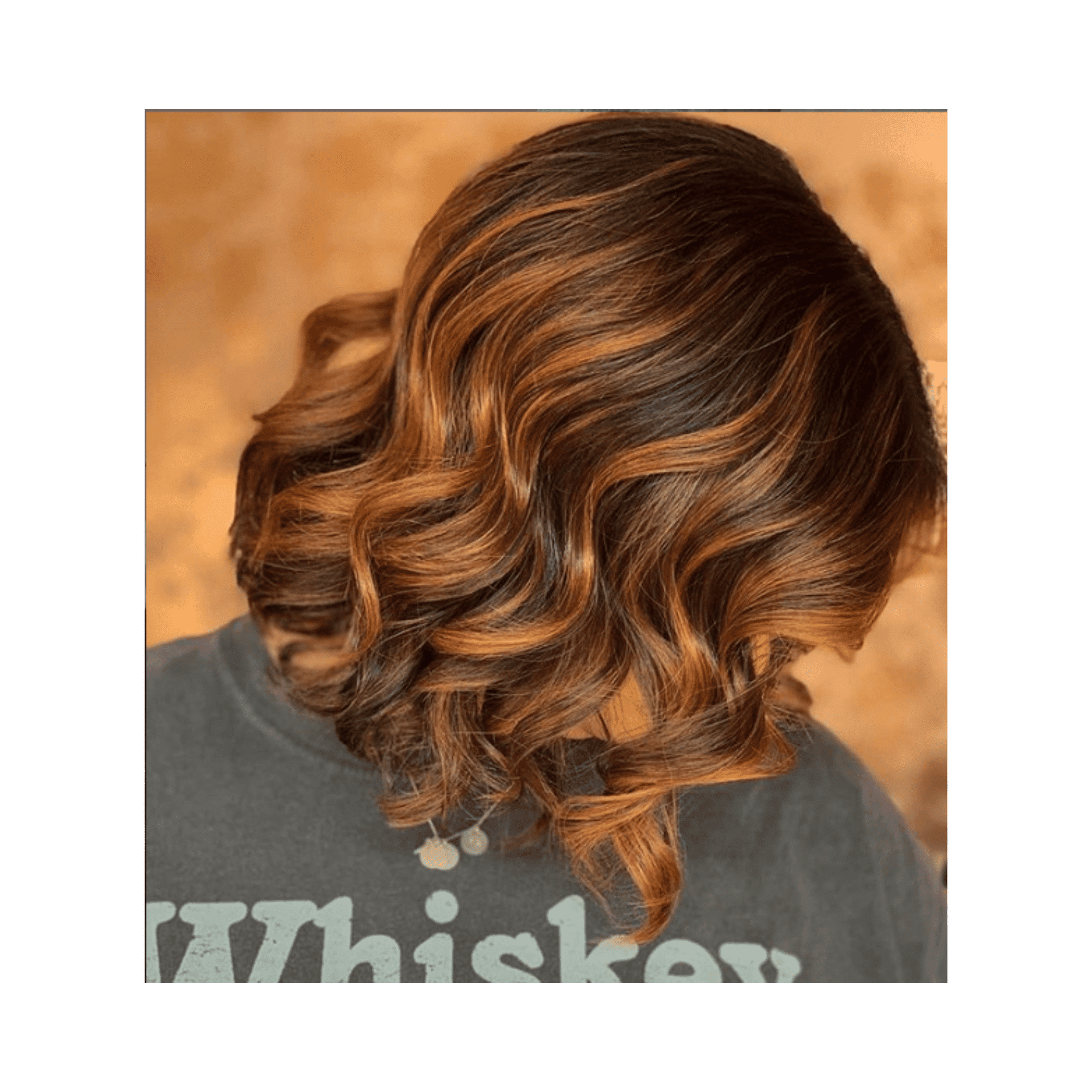 Short brown hair with copper highlights in loose curls against a warm, textured background.