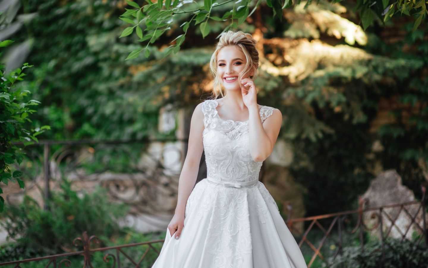 Bride in elegant white gown smiling in a lush garden setting.