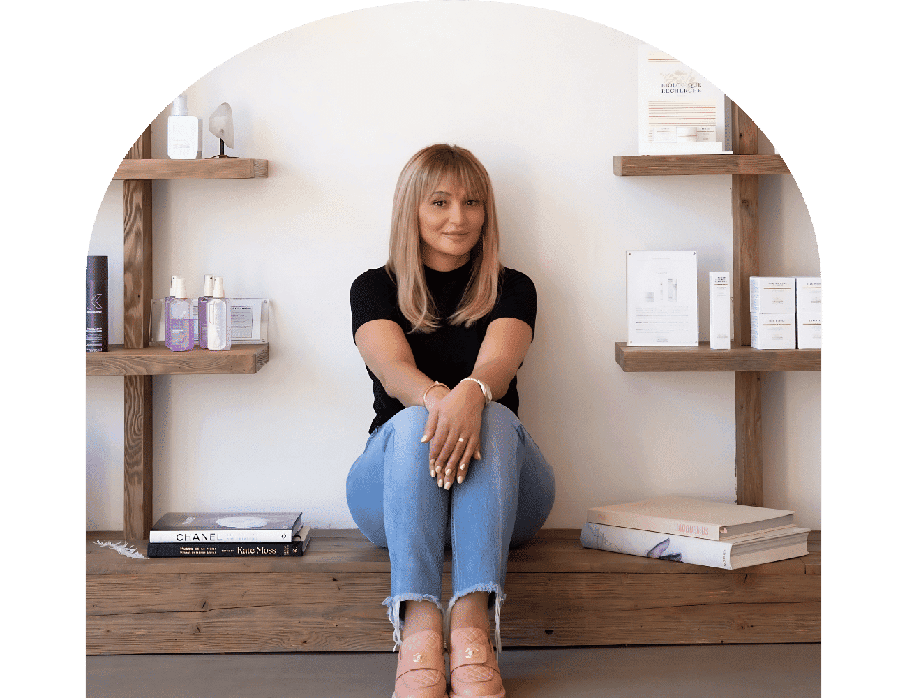 Woman sitting cross-legged on floor with shelves of beauty products in the background.