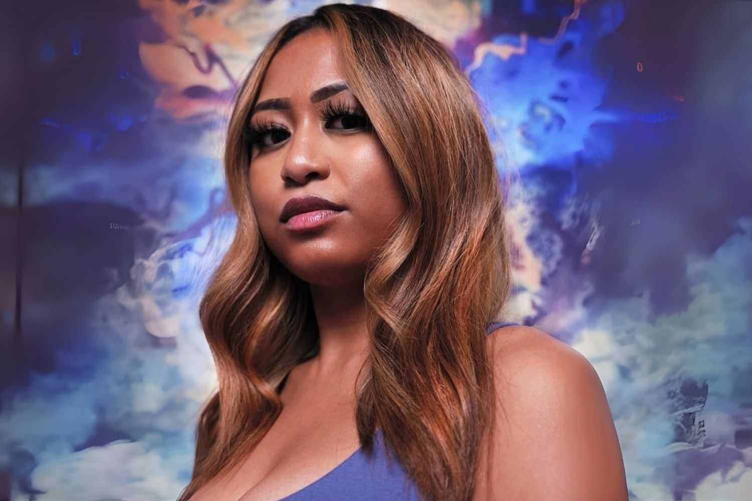 A woman stands in front of a colorful, dreamy cloud-like background.