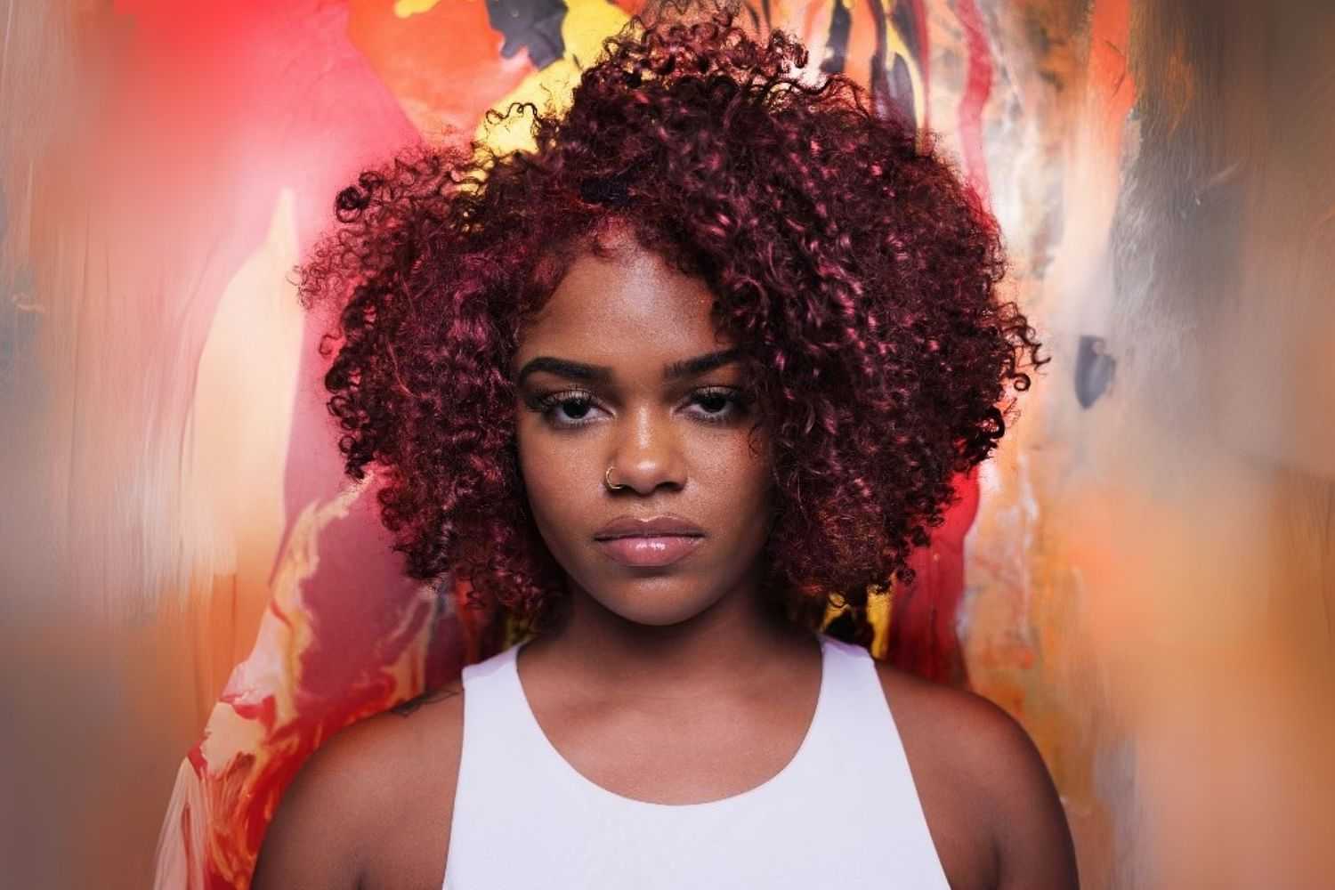 Young woman with curly hair standing against a vibrant, colorful abstract background.