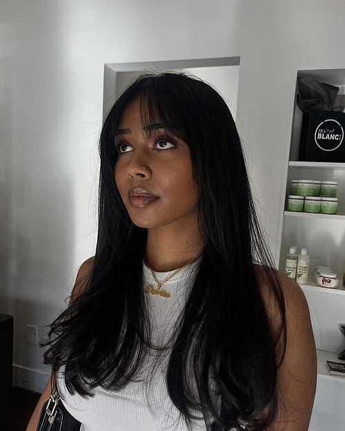 Woman with long black hair in white tank top inside a room.