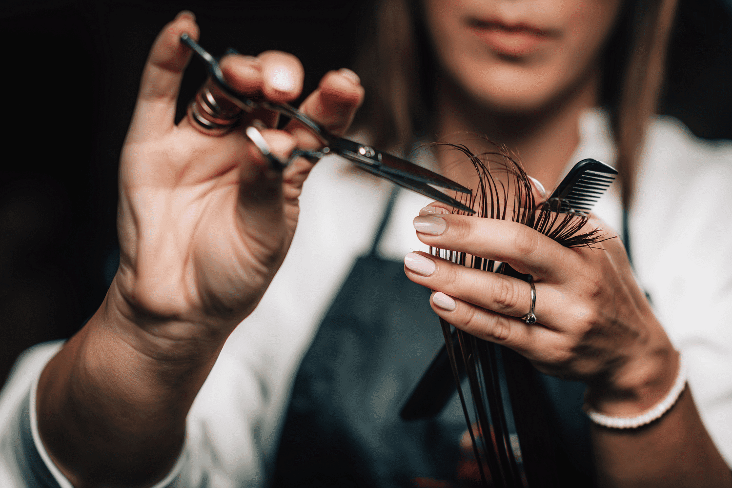 Hair stylist cutting hair with scissors, holding a comb in the other hand.