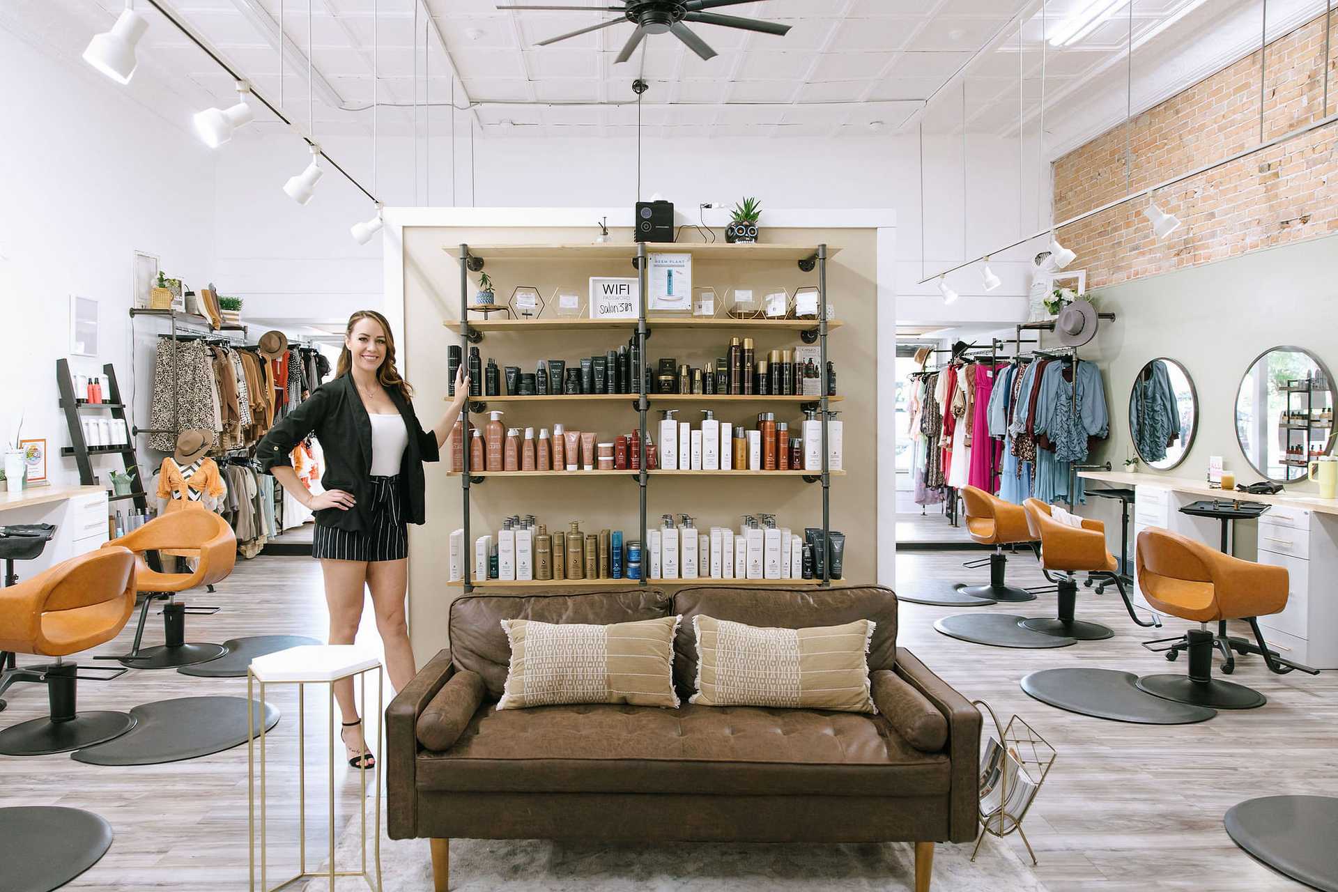 Woman standing in a stylish hair salon with products displayed and modern seating arrangements.