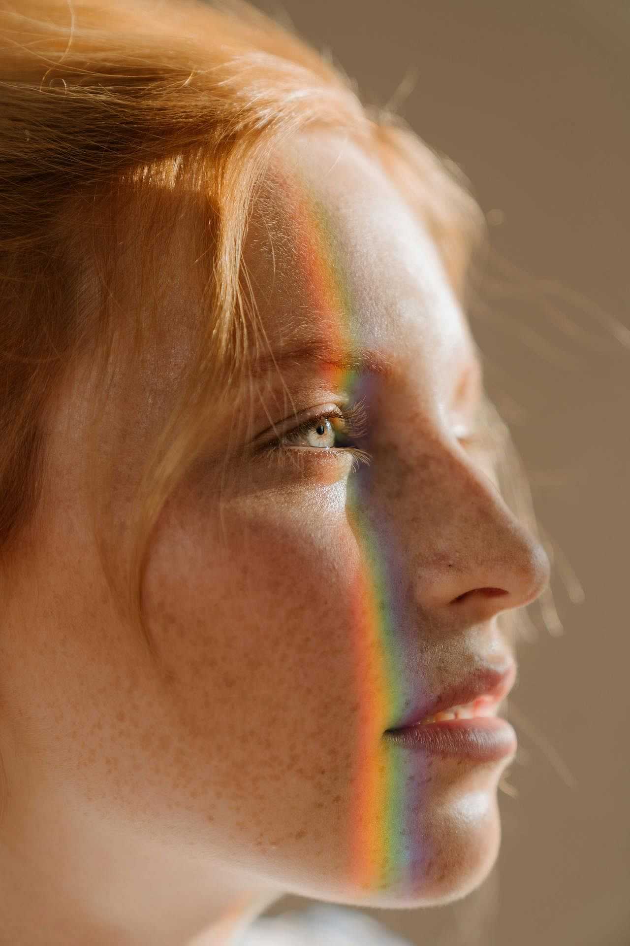 Close-up of a woman's face with a rainbow light across her forehead and cheek.