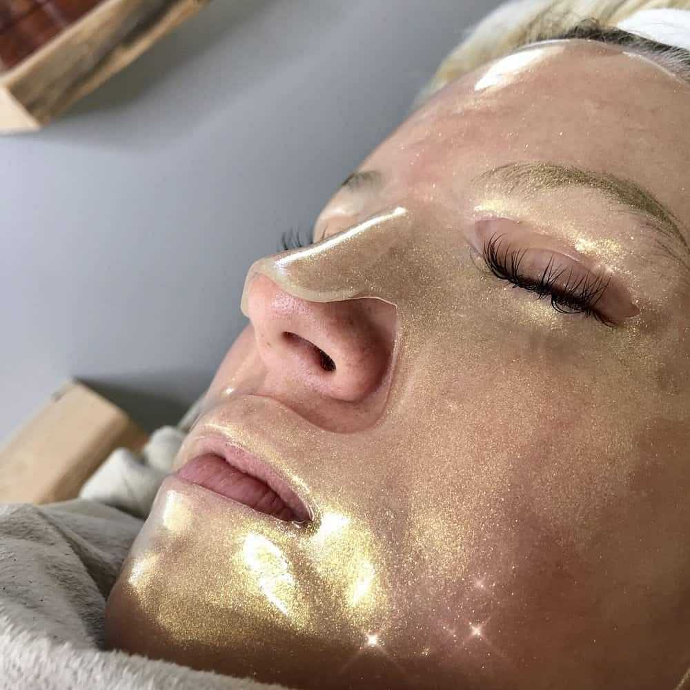 Person receiving a luxurious, gold face mask treatment at a spa.