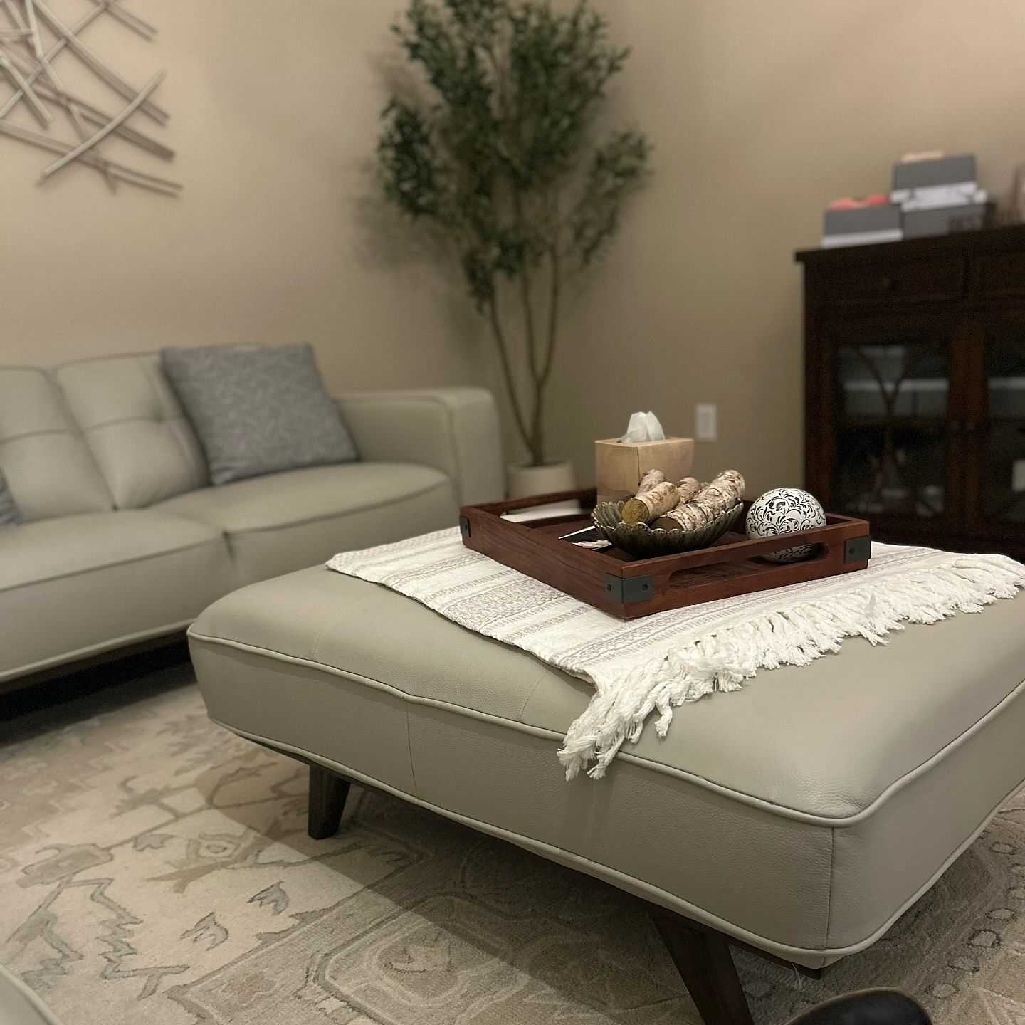 Cozy living room with beige sofa, ottoman, and decorative tray on a rug.