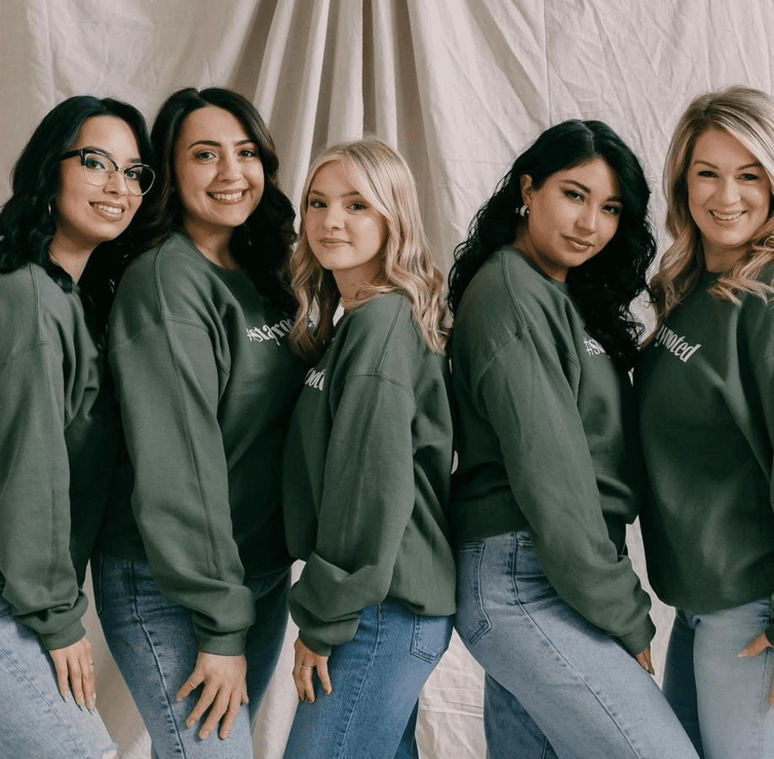 Women posing together in green sweatshirts and jeans, smiling at the camera.