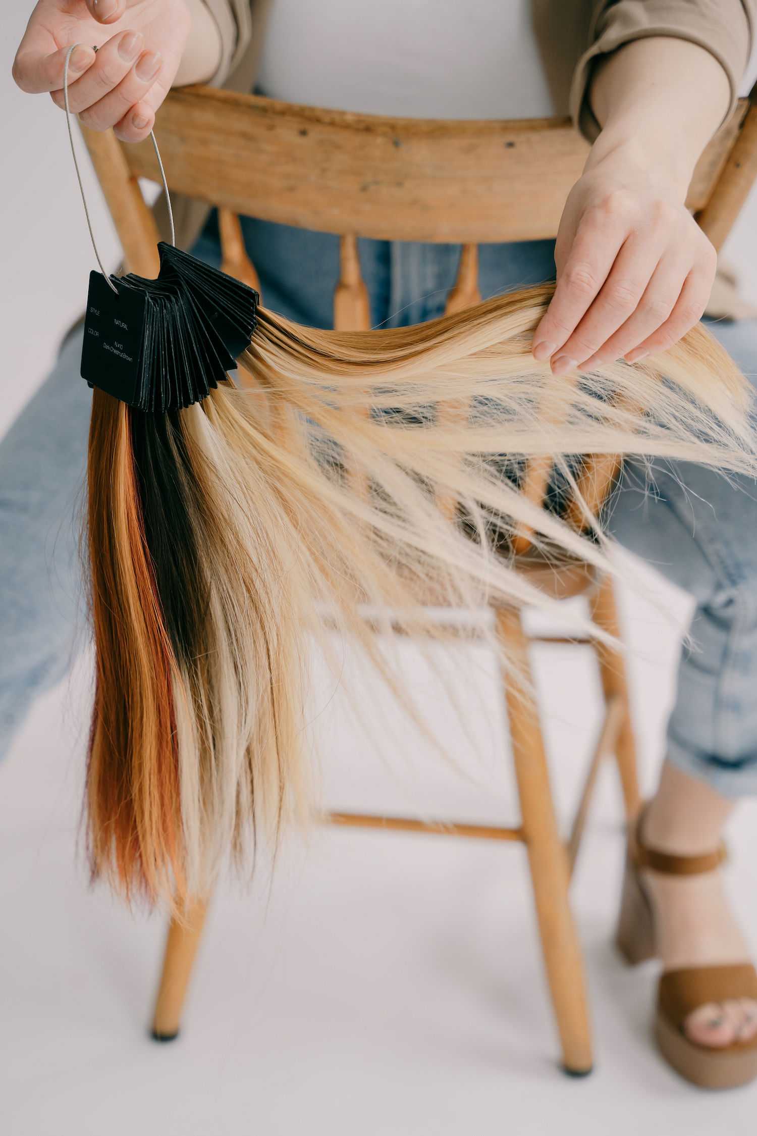 Hair color swatches displayed by a person sitting on a wooden chair.