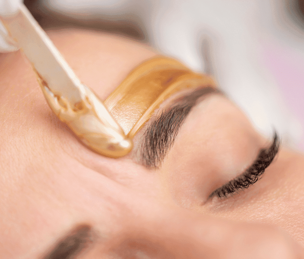 Eyebrow waxing in progress with warm wax applied to the skin above the brow.