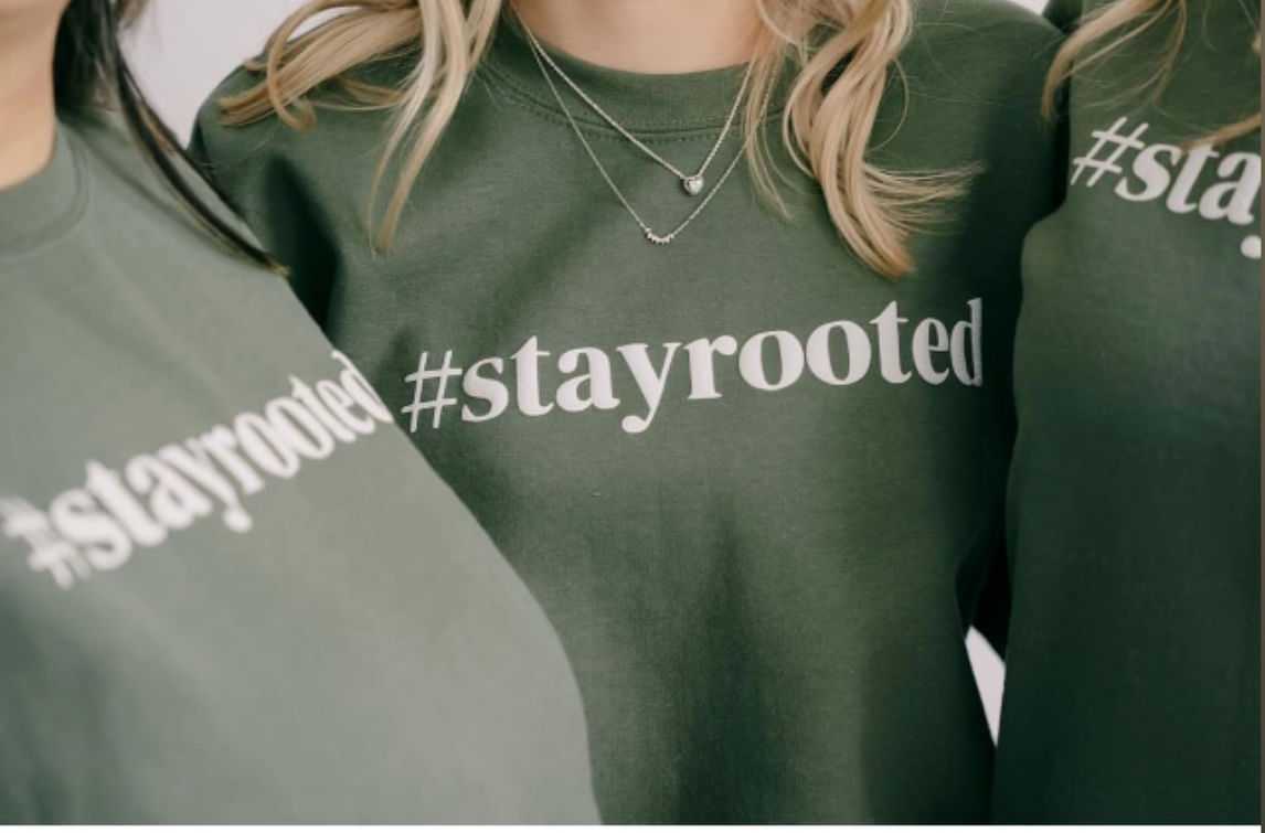 Three people wearing green sweatshirts with "#stayrooted" printed on the front.