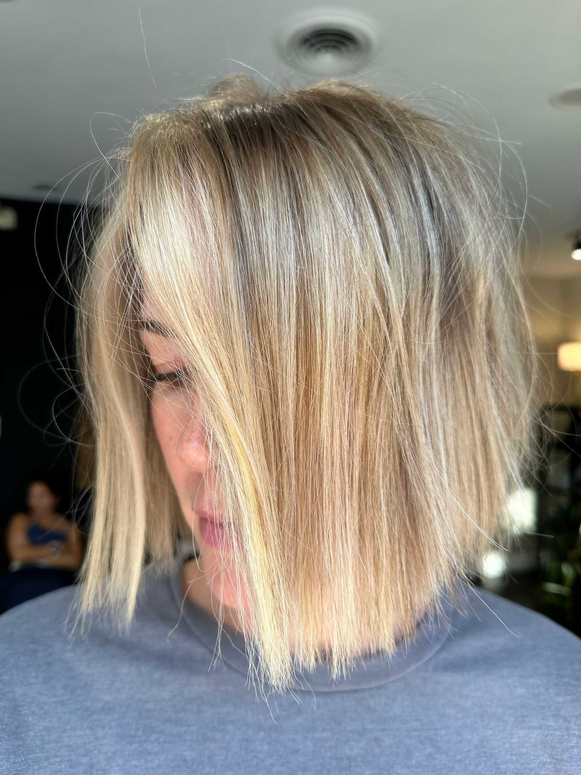 Blonde woman with a chin-length bob hairstyle, looking downwards in a salon setting.
