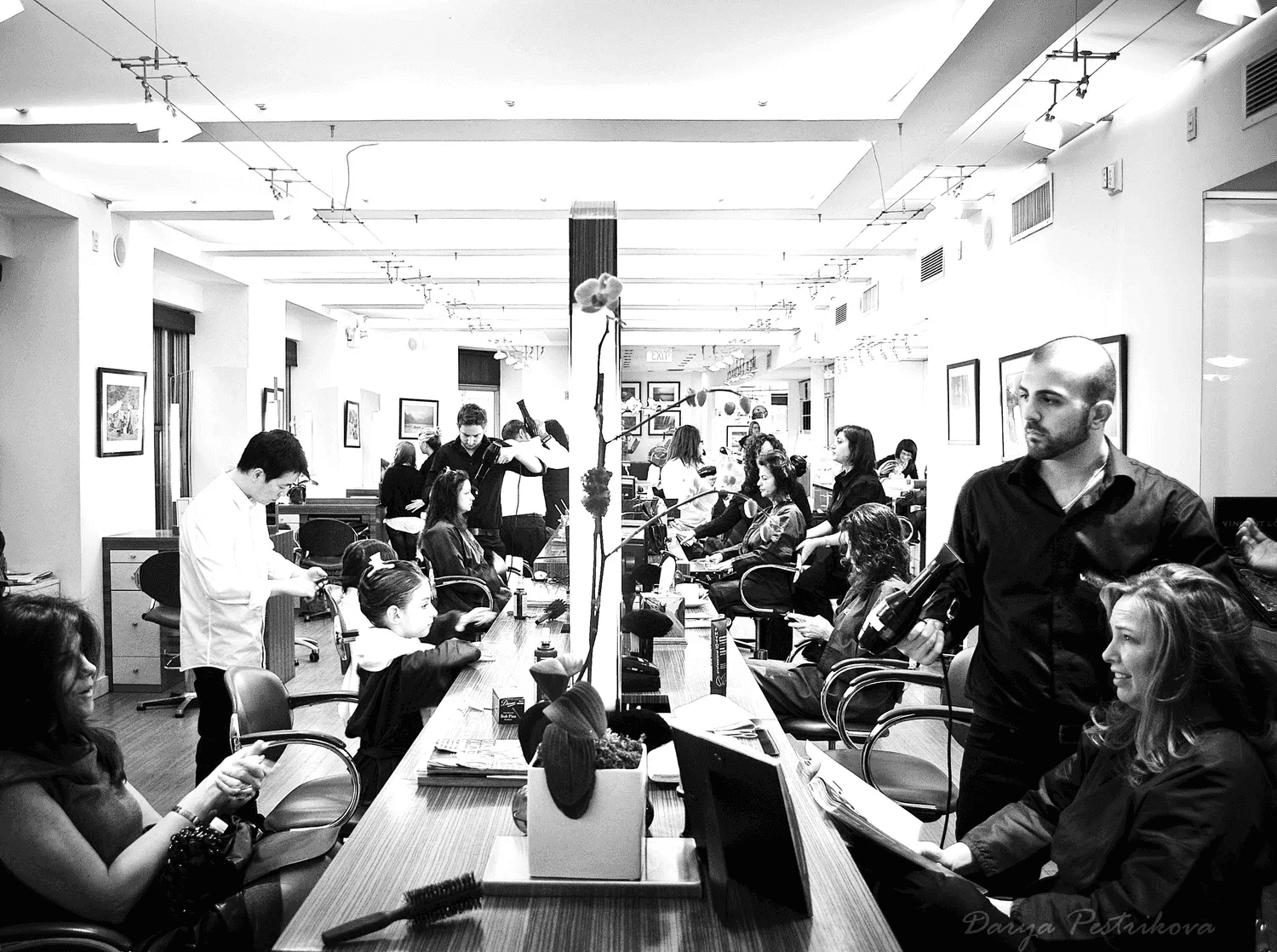 Bustling hair salon with clients getting haircuts and styling by several stylists.