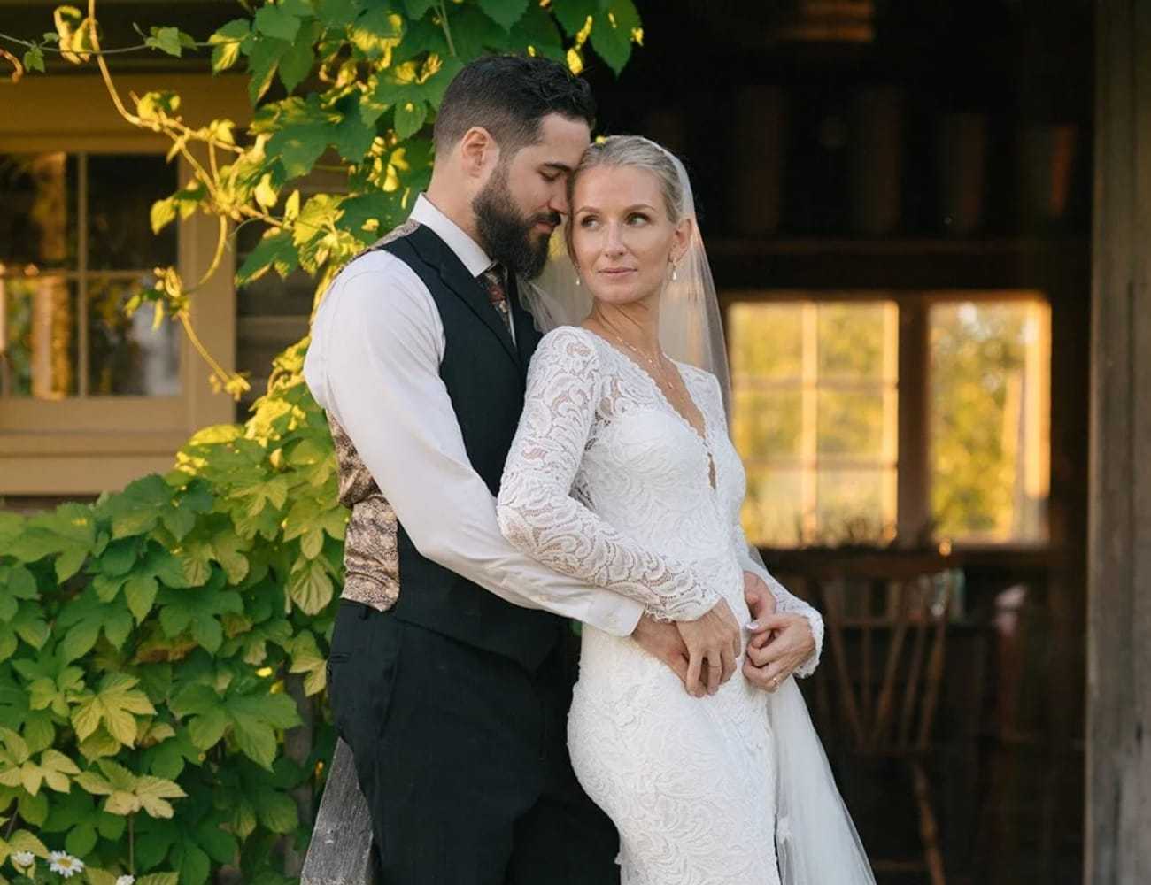 Bride and groom embrace in a garden setting outside a rustic building.