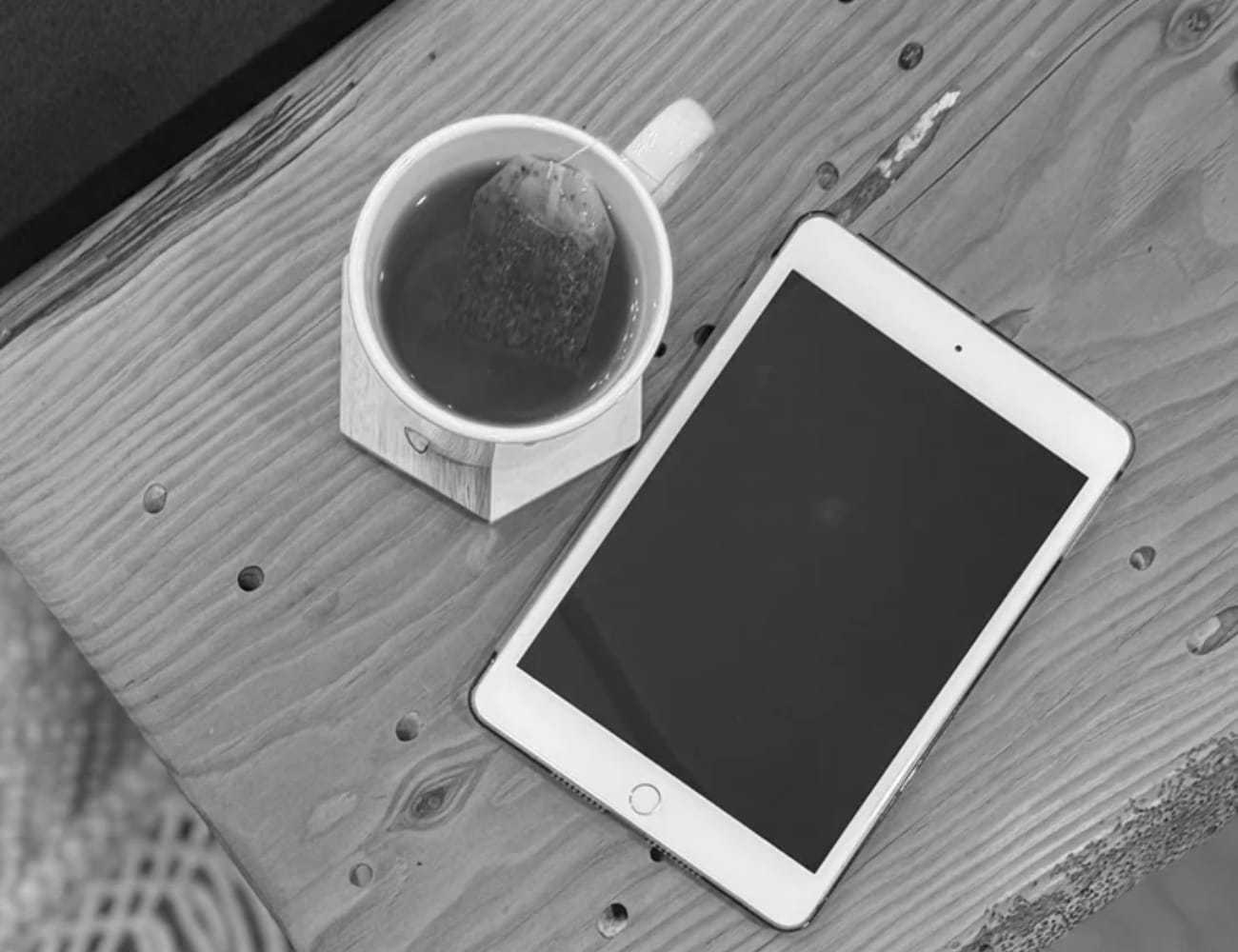 Cup of tea with a teabag beside a tablet on a wooden table.