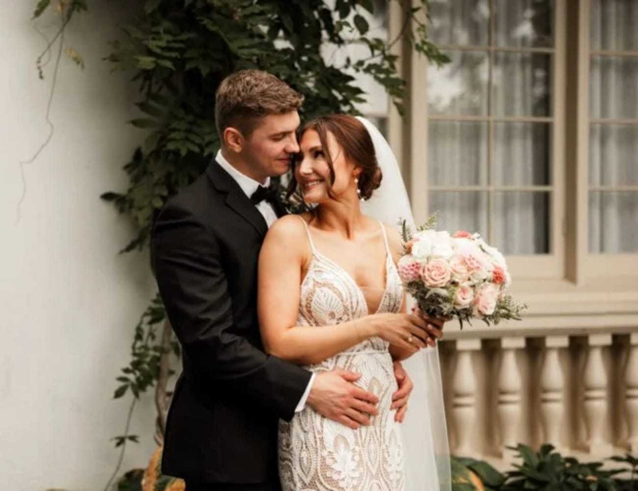Bride and groom smiling, embracing in front of a building with ivy.