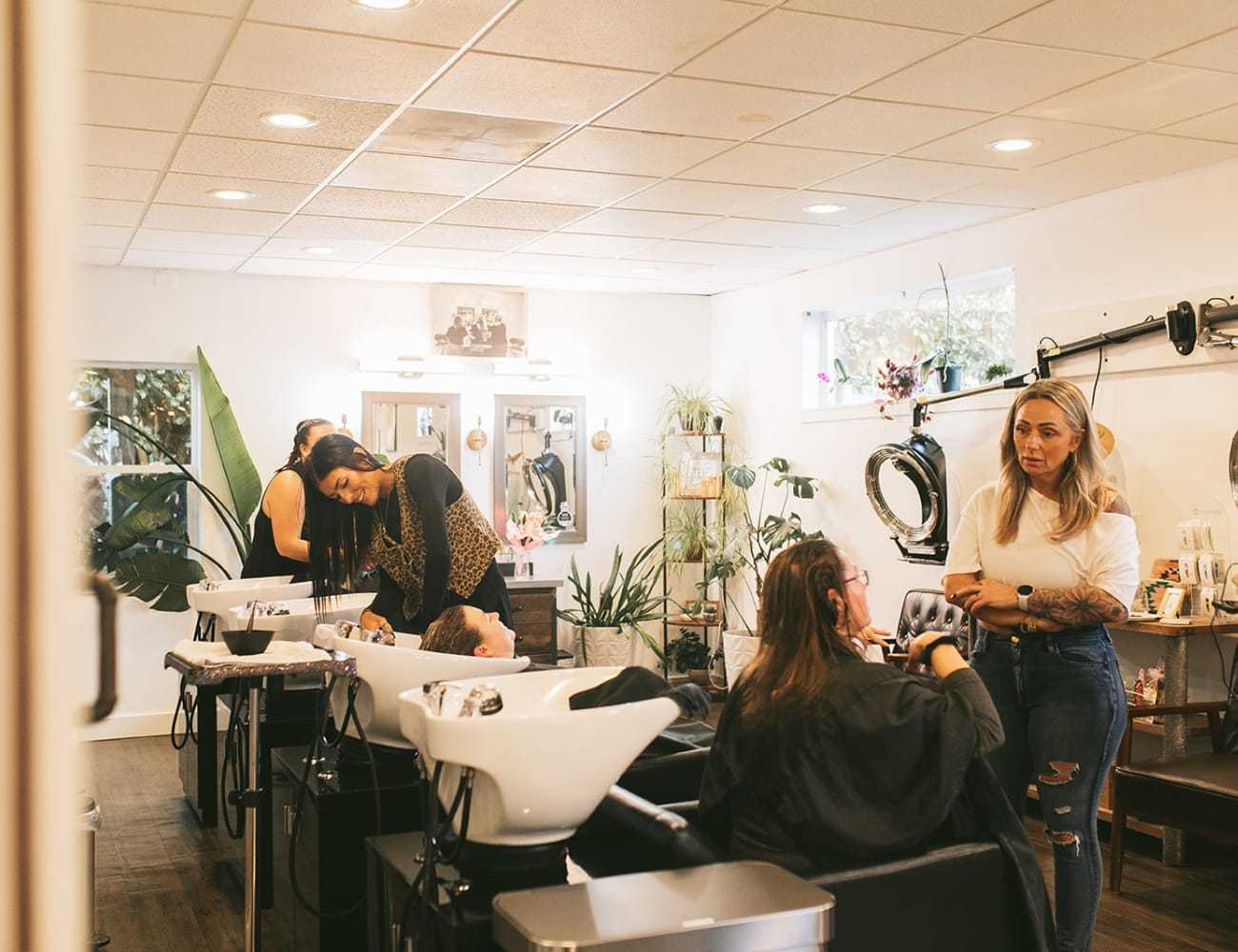 Salon interior with hairstylists working on clients under warm lighting.