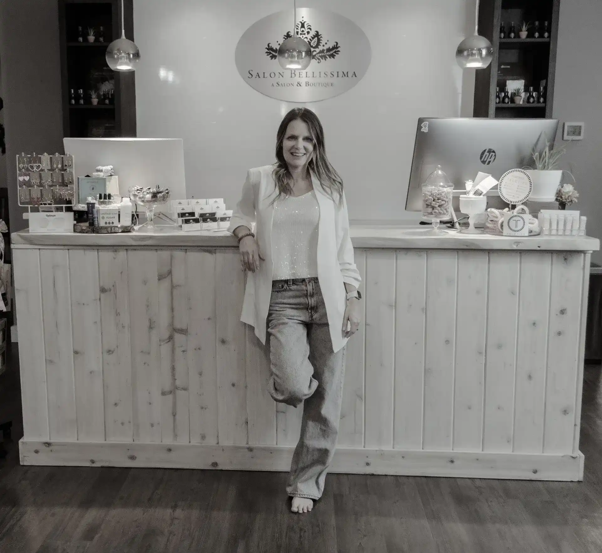 Woman standing at a salon reception desk, smiling.