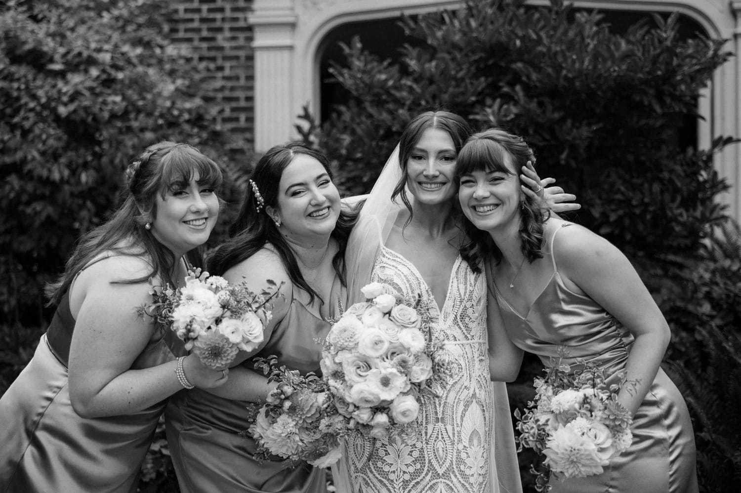 Bride and bridesmaids smiling with bouquets in an outdoor setting.