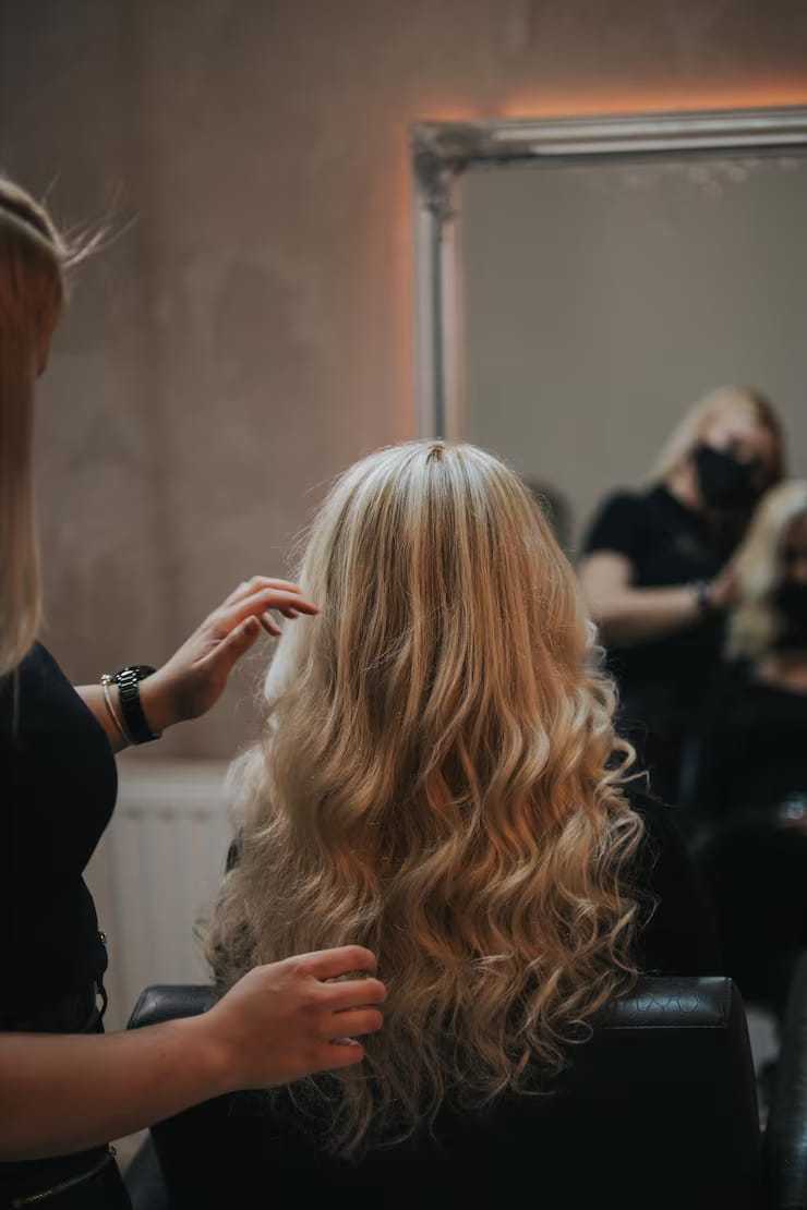 Blonde woman with wavy hair getting styled in a salon.