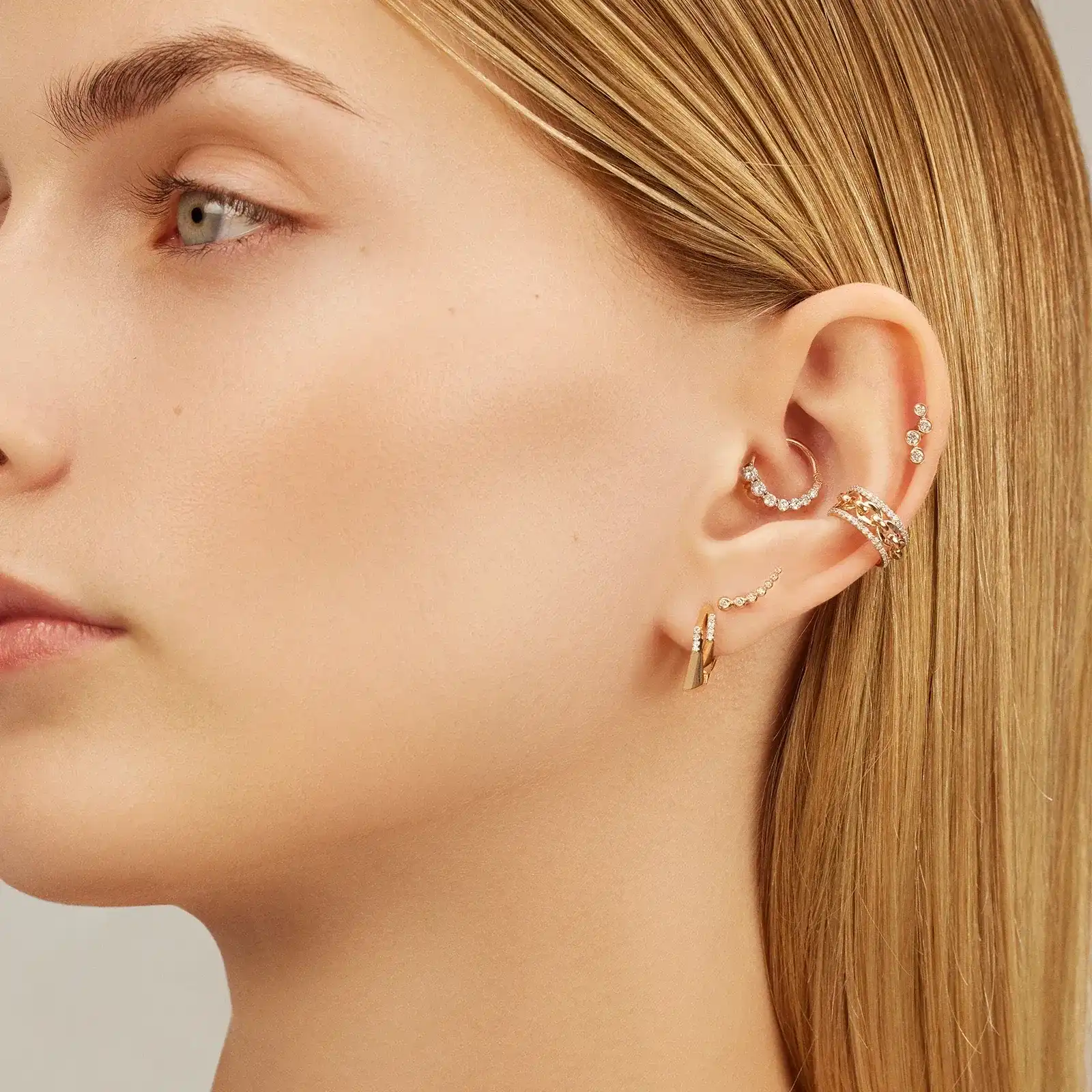 Close-up of woman's ear with multiple piercings, showcasing different gold jewelry pieces.