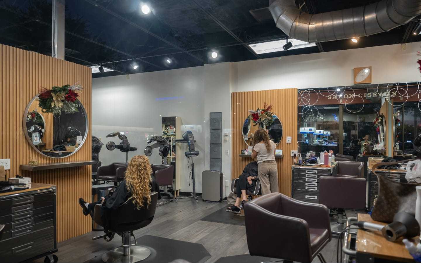 Hair salon with clients receiving services, holiday decorations, and modern interior.