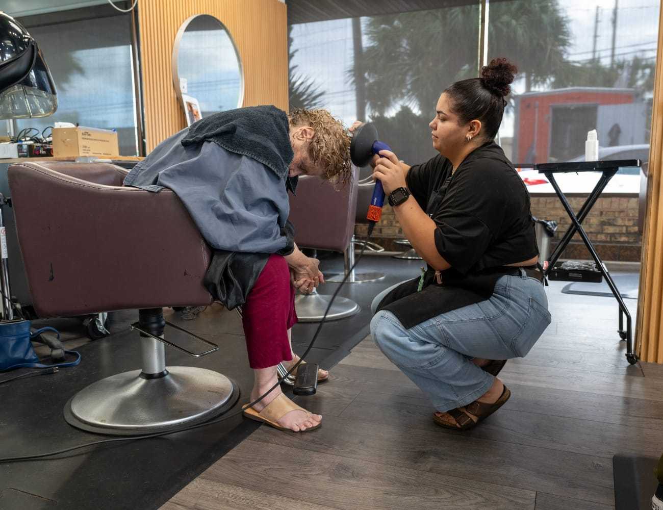 A hairstylist dries a seated client's hair in a salon.