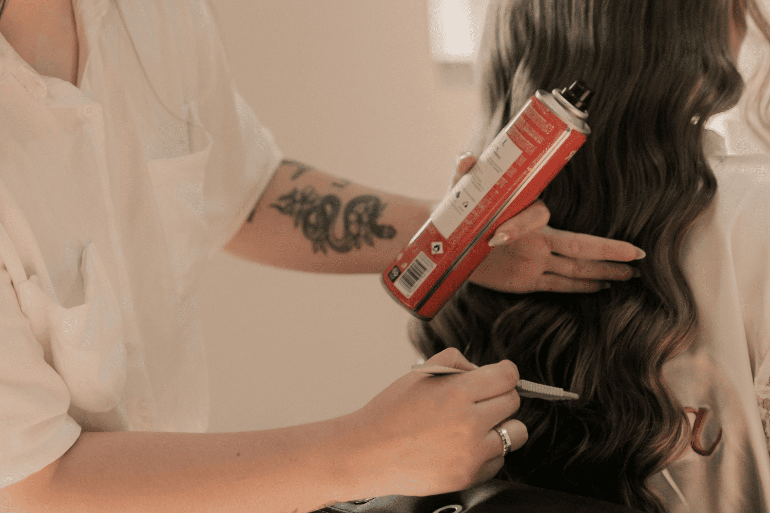 Person styling long hair with a curling iron and hair spray.