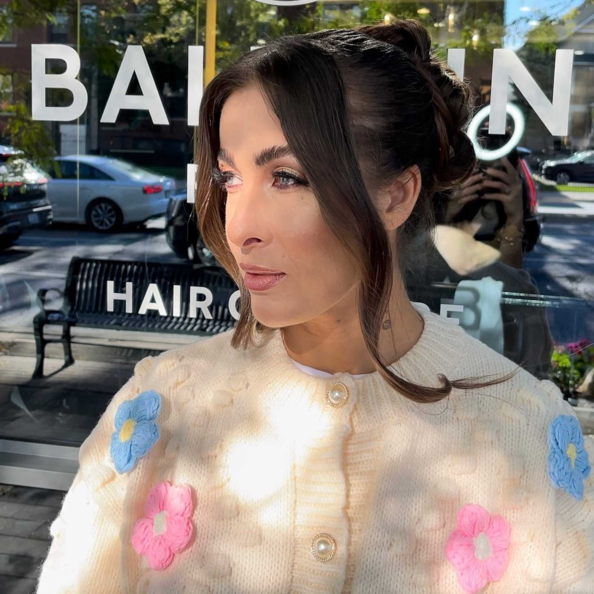 Woman with floral sweater outside a hair salon on a sunny day.
