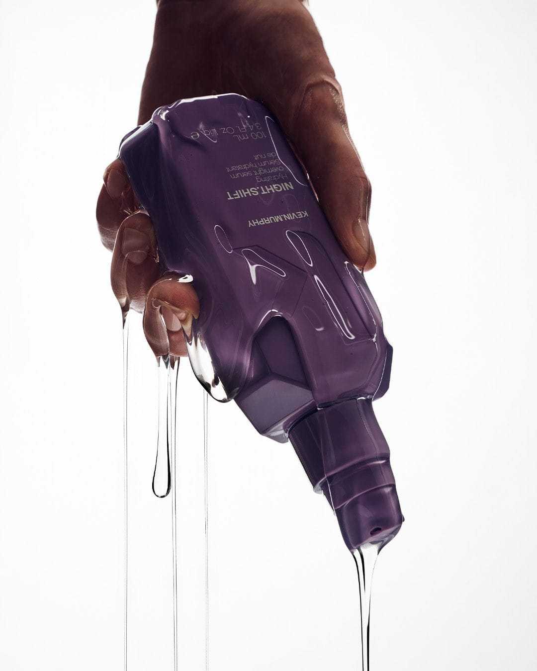 Dripping purple bottle of NIght Shift skincare serum held in a hand.