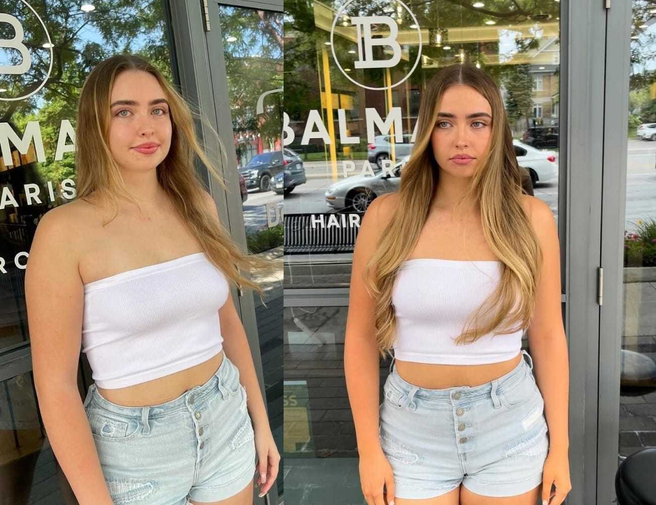 Woman with long hair in white top and denim shorts standing outside a hair salon.