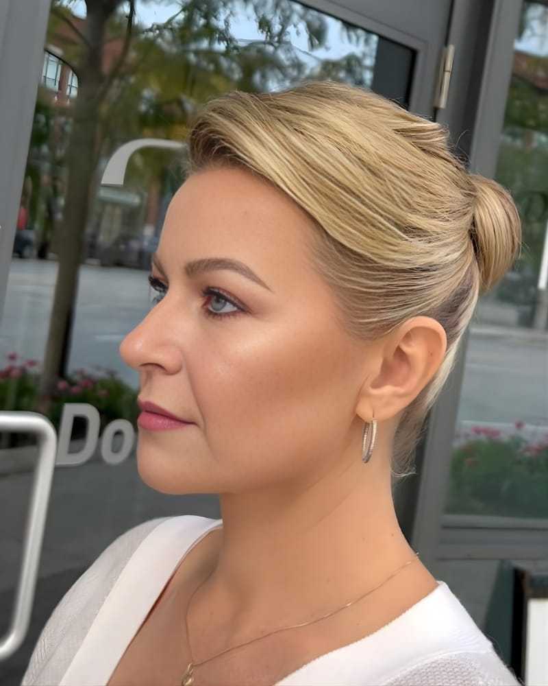 Profile of a woman with styled blonde hair, wearing hoop earrings and light makeup.