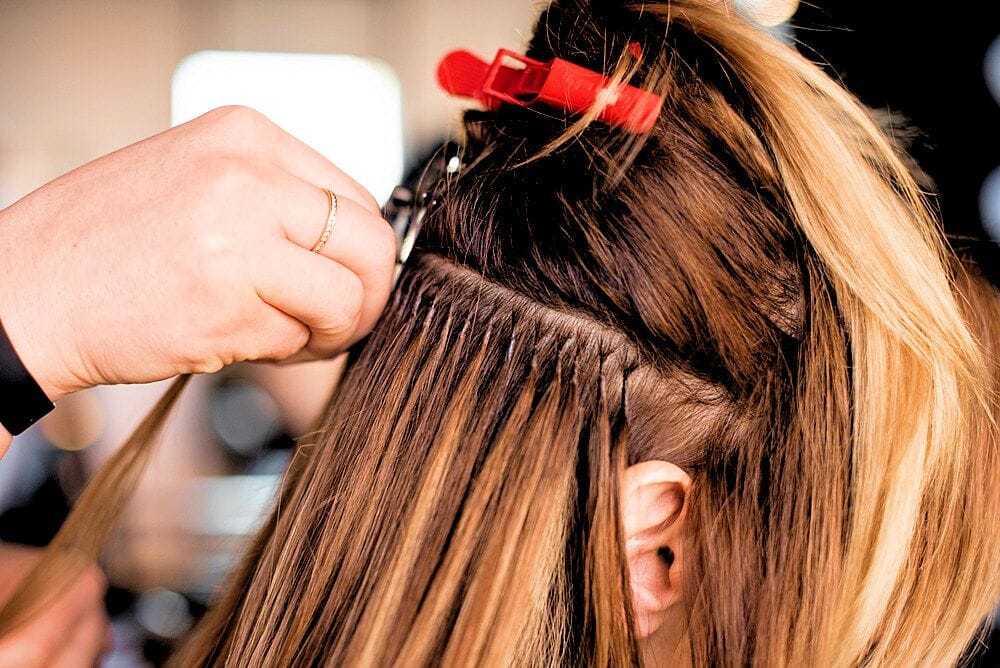 Hair stylist attaching extensions to blonde hair with a clip.