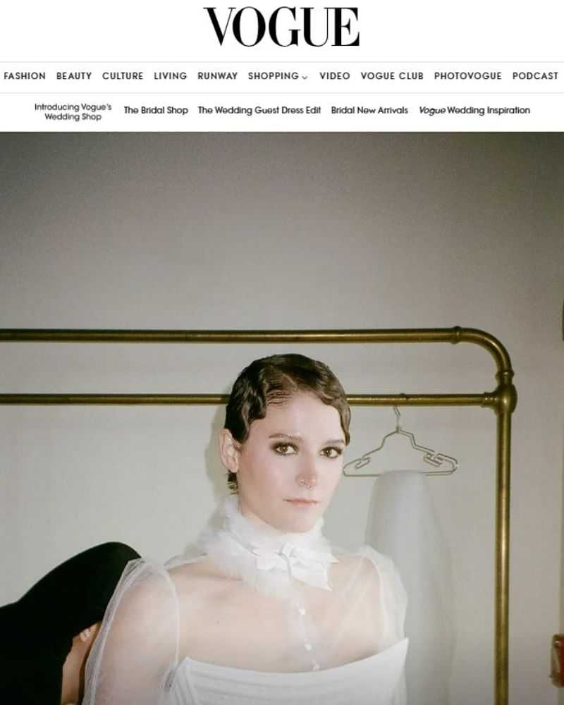 Woman in elegant white dress with wavy hair, standing in a softly lit room.