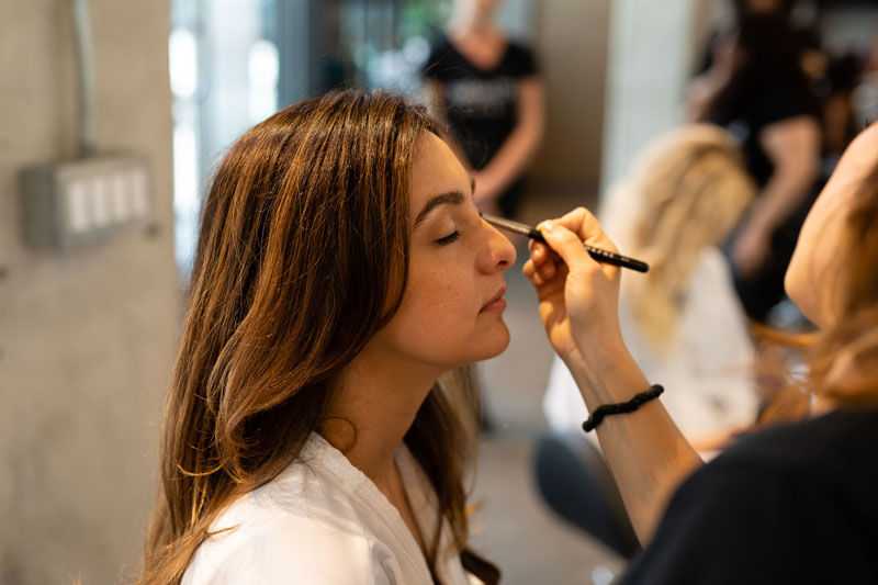 Makeup artist applying eyeshadow to a woman in a salon setting.