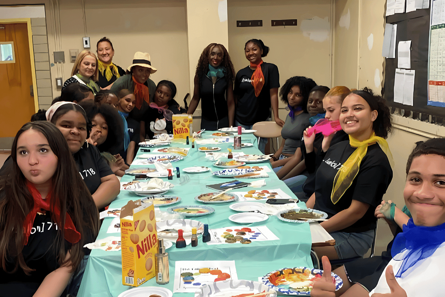 Group of people at a table painting and smiling together in a classroom setting.