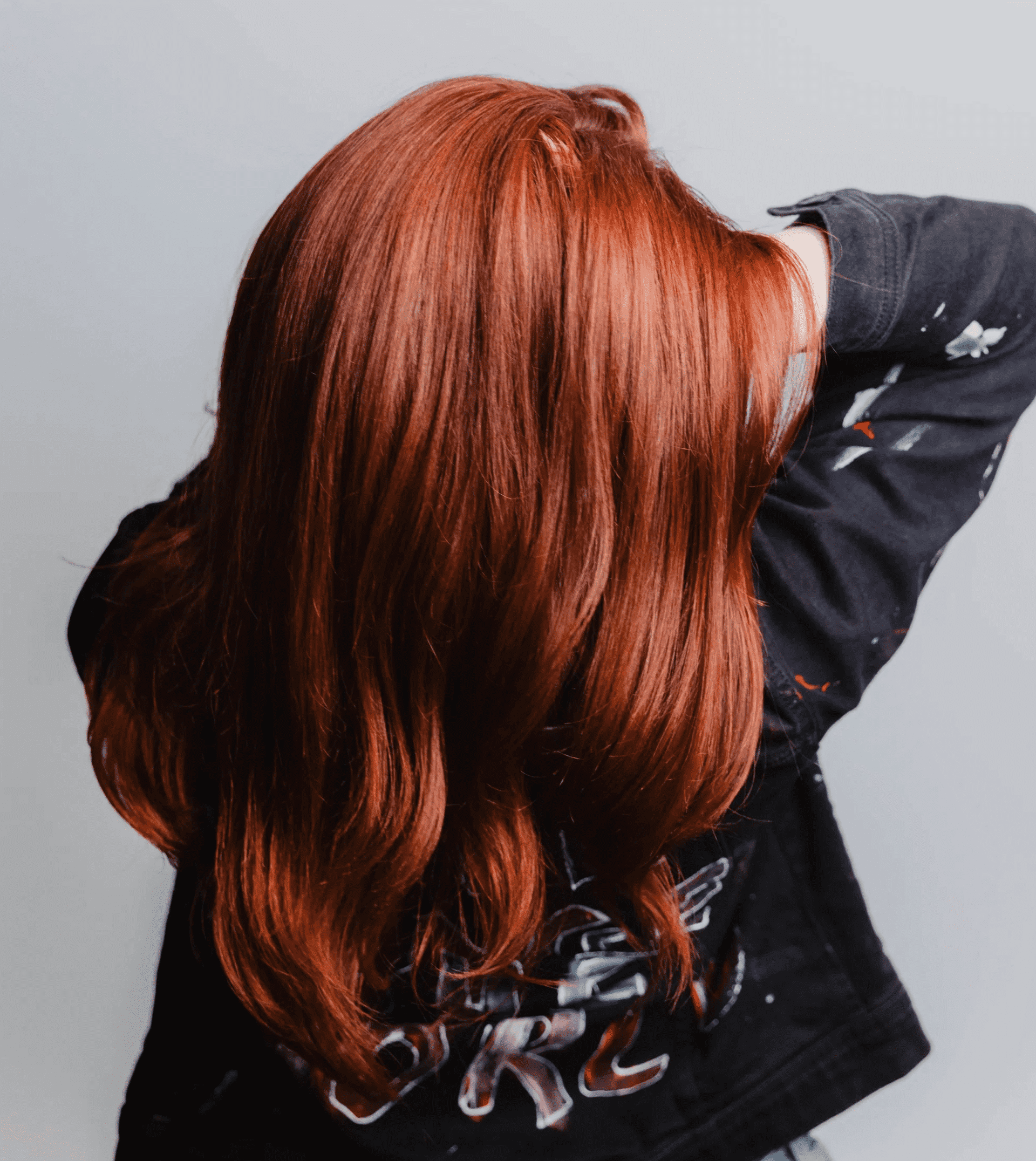 Red-haired person with long hair facing away, against a light gray background.