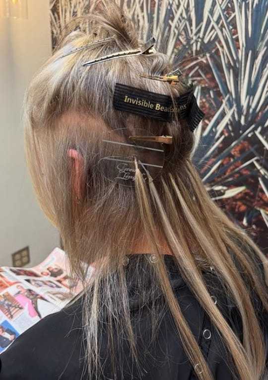 Hair extensions being applied to a person's head in a salon setting.