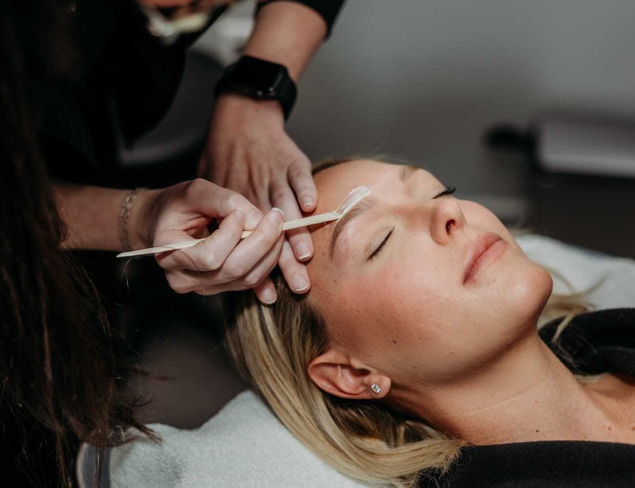 Woman receiving eyebrow treatment with a brush in a spa setting.