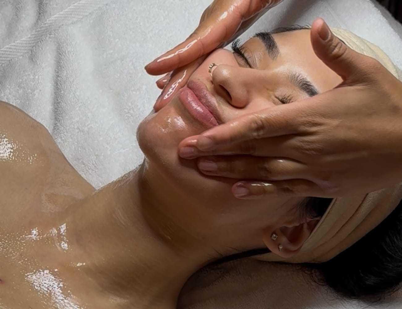 Facial massage therapy with oil on a relaxed woman lying on a spa bed.
