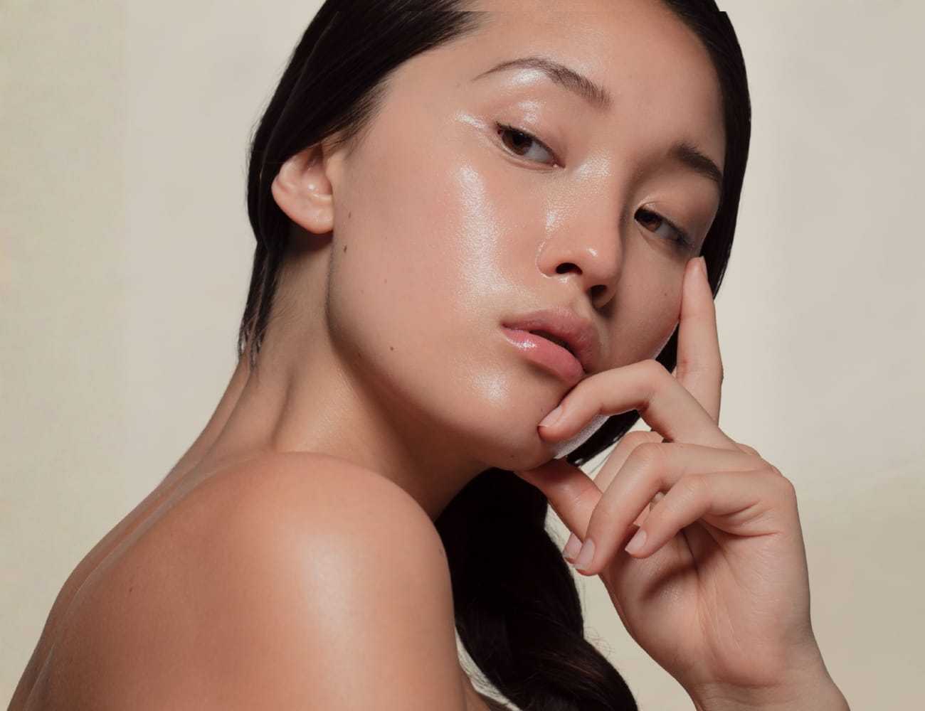 Elegant woman with glowing skin, posing gracefully against a neutral background.
