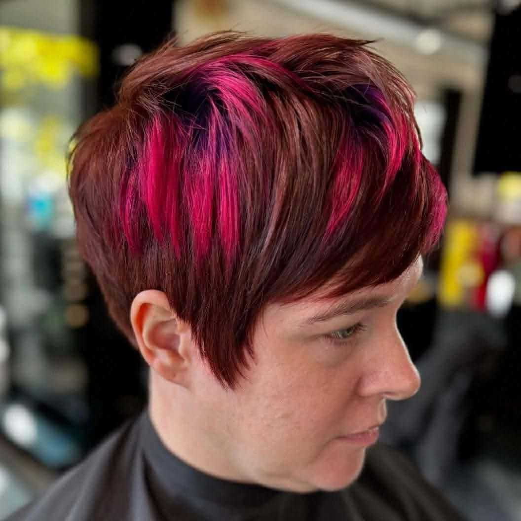 Short red hairstyle with vibrant pink streaks in a modern salon setting.