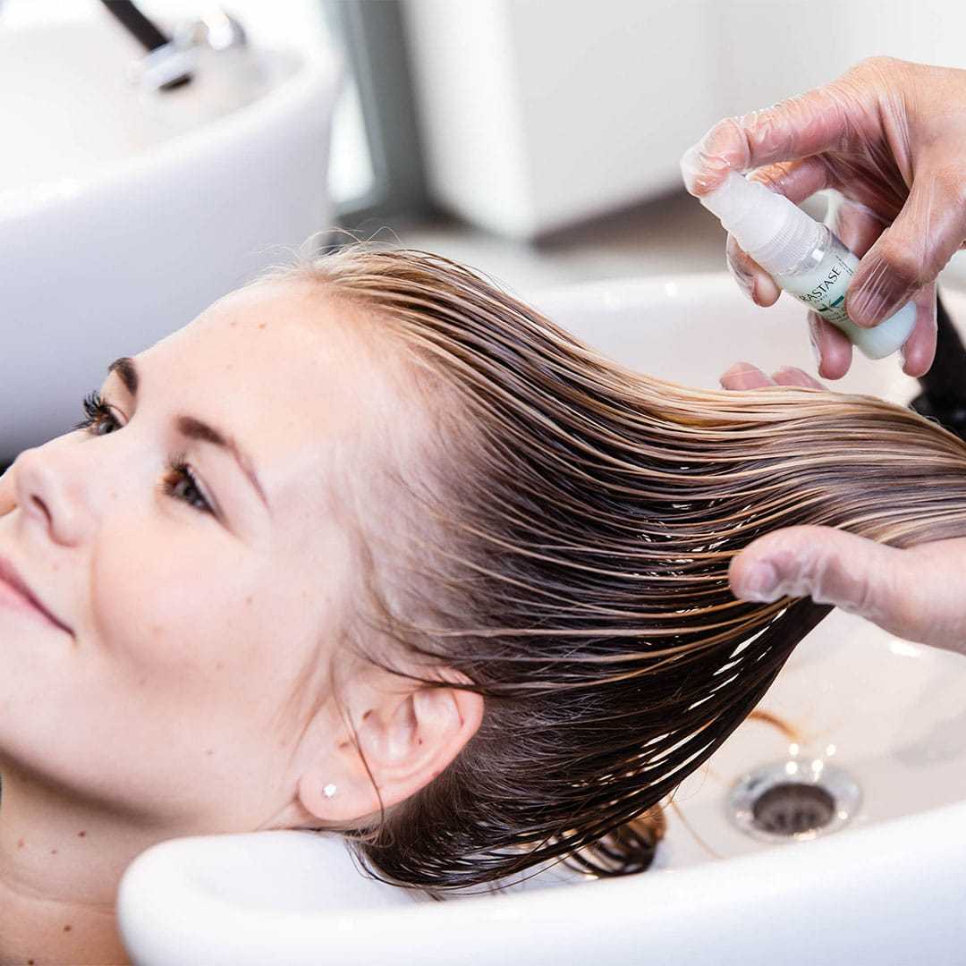 Hair treatment being applied to a woman's wet hair in a salon setting.