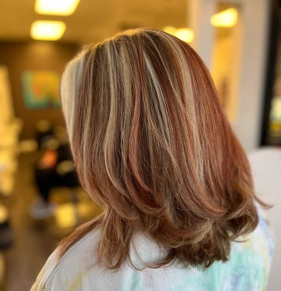 Elegant layered hairstyle with copper and blonde highlights in a salon setting.